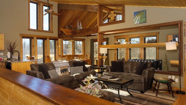 A spacious living room with a high ceiling, wooden beams, and large windows. There is a fireplace, a coffee table, and a sofa set. - 701B Quail Family & pet friendly 3 bedroom rental private hot tub (Fraser)