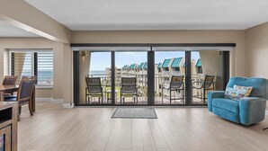 A spacious living room with a large sliding glass door leading to a balcony with outdoor furniture. - Fantastic Oceanview Condo Errol by the Sea 515 (New Smyrna Beach)