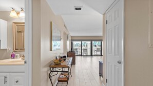 A hallway with a sink, mirror, and table with chairs. There is a door on the right and a window at the end of the hallway. - Fantastic Oceanview Condo Errol by the Sea 515 (New Smyrna Beach)