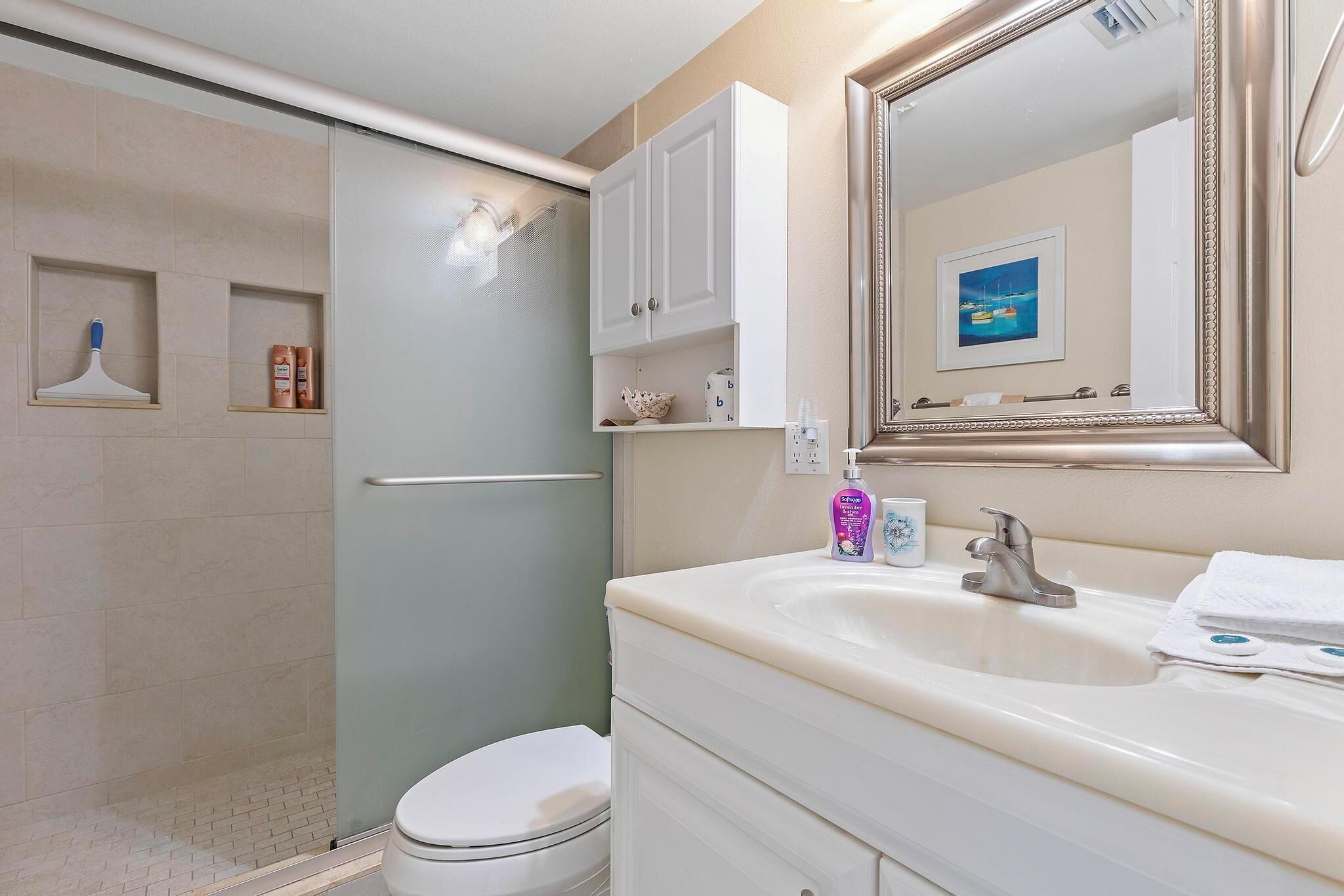 Une salle de bain équipée d’une douche, de toilettes, d’un lavabo et d’un miroir agrémenté d’un tableau encadré.