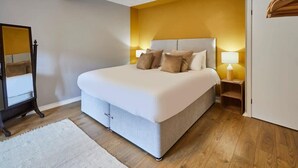 A bedroom with a large bed, bedside lamps, a wooden floor, and a mirror. - Host & Stay | Stone Row (Saltburn-by-the-Sea)