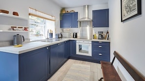 A modern kitchen with blue cabinets, a stainless steel range hood, and a built-in oven. - Host & Stay | Stone Row (Saltburn-by-the-Sea)