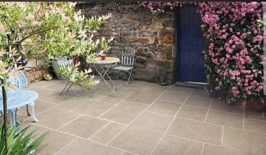 Une terrasse avec un sol en pierre, une table ronde et deux chaises.