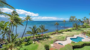 A pool area with a view of the ocean, surrounded by palm trees and a well-maintained lawn.
