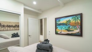 A hotel room with a bed, a painting of a beach scene, and a door leading to another room.