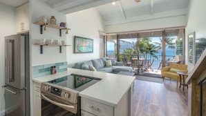 A modern kitchen with a central island, a dining area with a view of the ocean, and a living space with a sofa and chairs.