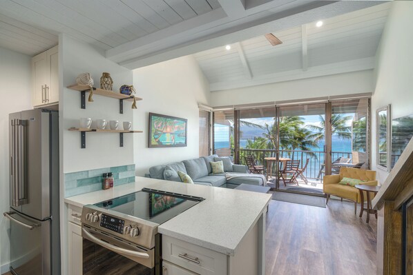 A modern kitchen with a central island, a dining area with a view of the ocean, and a living space with a sofa and chairs.