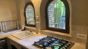 A kitchen with two sinks, a gas stove, and arched windows overlooking a stone wall and greenery. - Appartement Proche de la Plage (Cavalaire-sur-Mer)