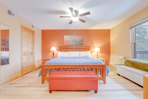 Ein Schlafzimmer mit einem Bett, Nachttischlampen, einem Deckenventilator, einem Fenster und Blick auf Bäume.