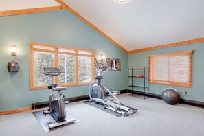 A home gym with two stationary bikes, a yoga mat, a kettlebell, and a large exercise ball.