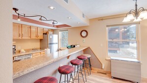 A kitchen with wooden cabinets, a granite countertop, and a stainless steel refrigerator. There are four bar stools with red and black checkered upholstery. - Updated 1st Floor End Unit Near Main Street (Frisco)