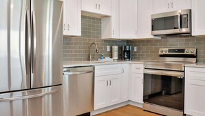 A modern kitchen with stainless steel appliances, white cabinets, and a tiled backsplash. - Beachfront, Amazing Views, Elevator ~ GW 2 (St. Joe Beach)