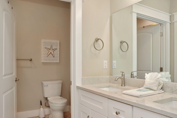 Baño con inodoro, lavabo y espejo. Hay una toalla sobre el lavabo y una decoración de estrella de mar en la pared.