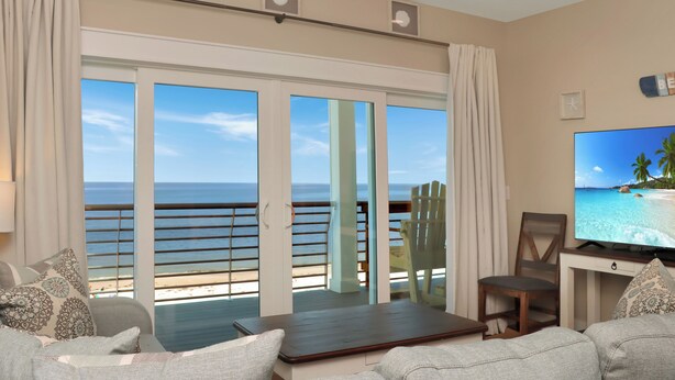 A living room with a large TV, a sofa, and a view of the ocean through a sliding glass door. - Beachfront, Amazing Views, Elevator ~ GW 2 (St. Joe Beach)