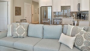 A modern living room with a grey sectional sofa, a dining area with a wooden table and chairs, and a kitchen with white cabinets and stainless steel appliances. - Beachfront, Amazing Views, Elevator ~ GW 2 (St. Joe Beach)