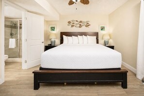 A bedroom with a large bed, a wooden headboard, two bedside tables with lamps, a wall-mounted artwork, and a glass shower enclosure. - Beachfront Condo at Phoenix III! (Orange Beach)