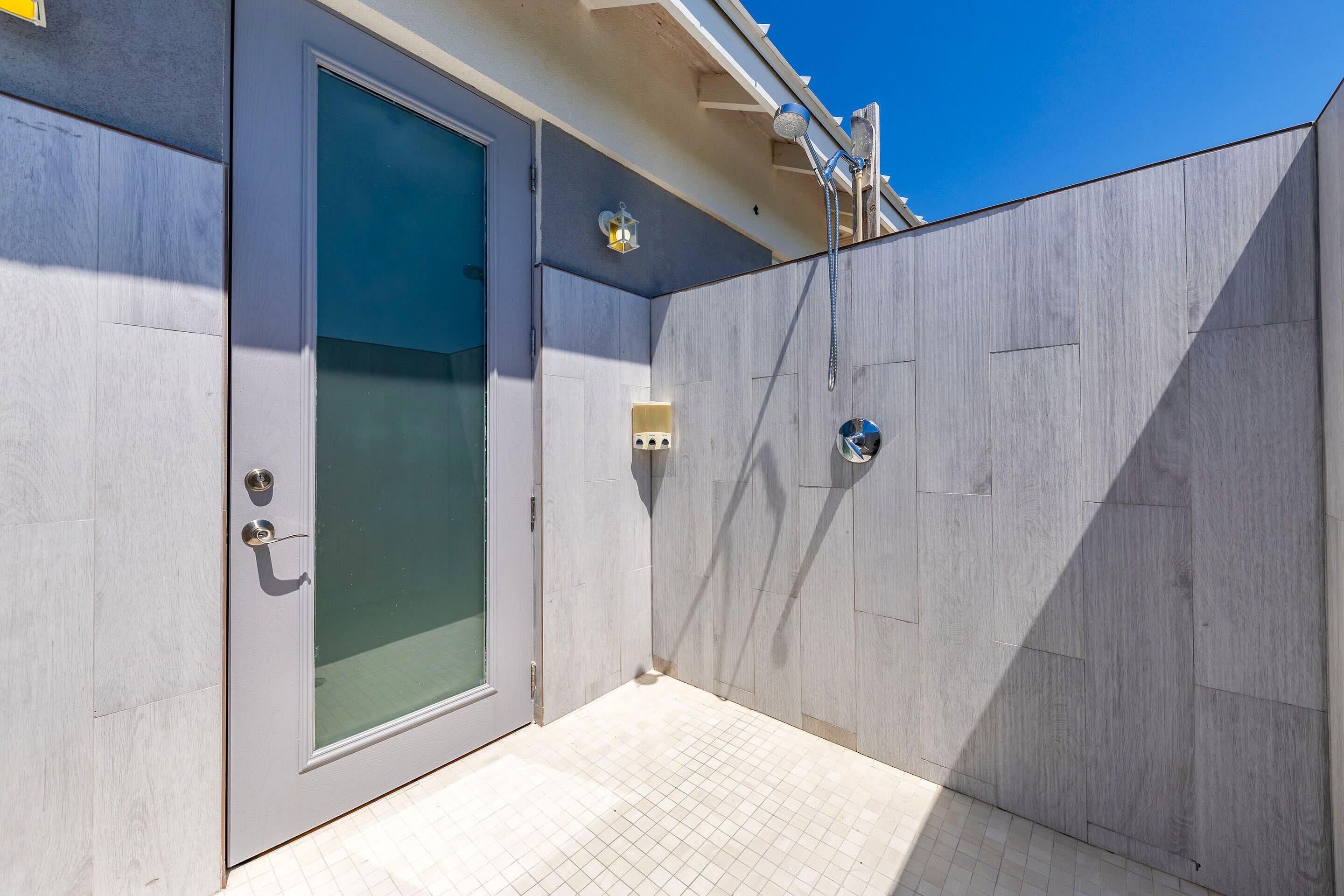 Un área de ducha exterior moderna con puerta de cristal, cabezal de ducha metálico e iluminación en la pared.