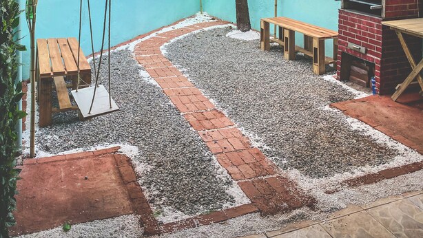 Un patio con un columpio, un banco de madera, una parrilla de ladrillo y un árbol.