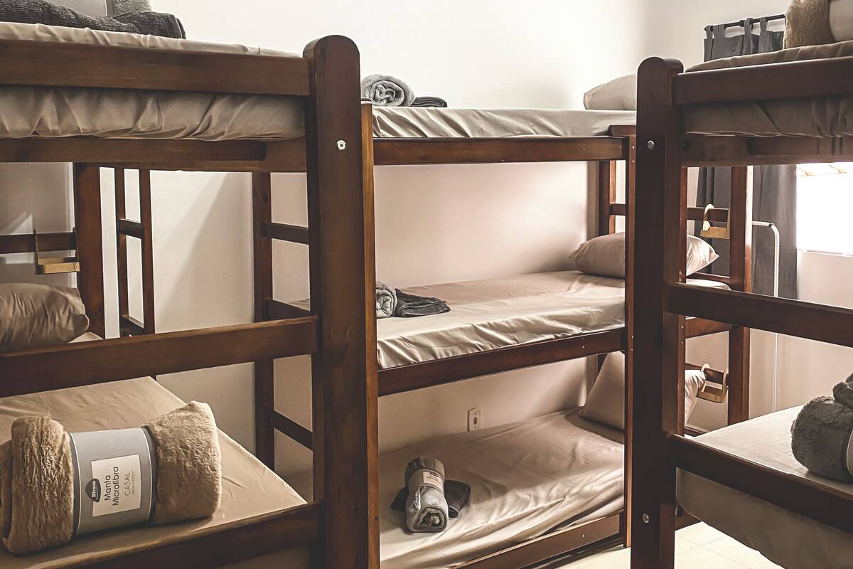 A bunk bed room with wooden frames, a mattress on the bottom bunk, and a rolled-up blanket on the top bunk.