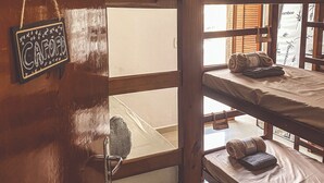 Habitación con literas de madera, un letrero en la pared y una ventana con contraventanas de madera.