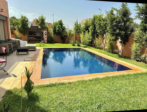 A rectangular swimming pool with a wooden border, surrounded by a well-maintained lawn and various plants.