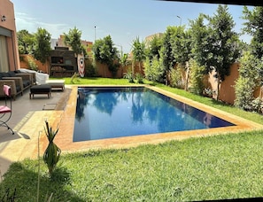 Une piscine rectangulaire bordée de bois, entourée d’une pelouse bien entretenue et de diverses plantes.