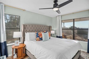 Un dormitorio con una cama grande, un ventilador de techo y dos ventanas.