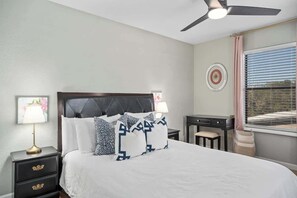 Un dormitorio ordenado con cama, mesitas de noche, un escritorio y una ventana con persianas.