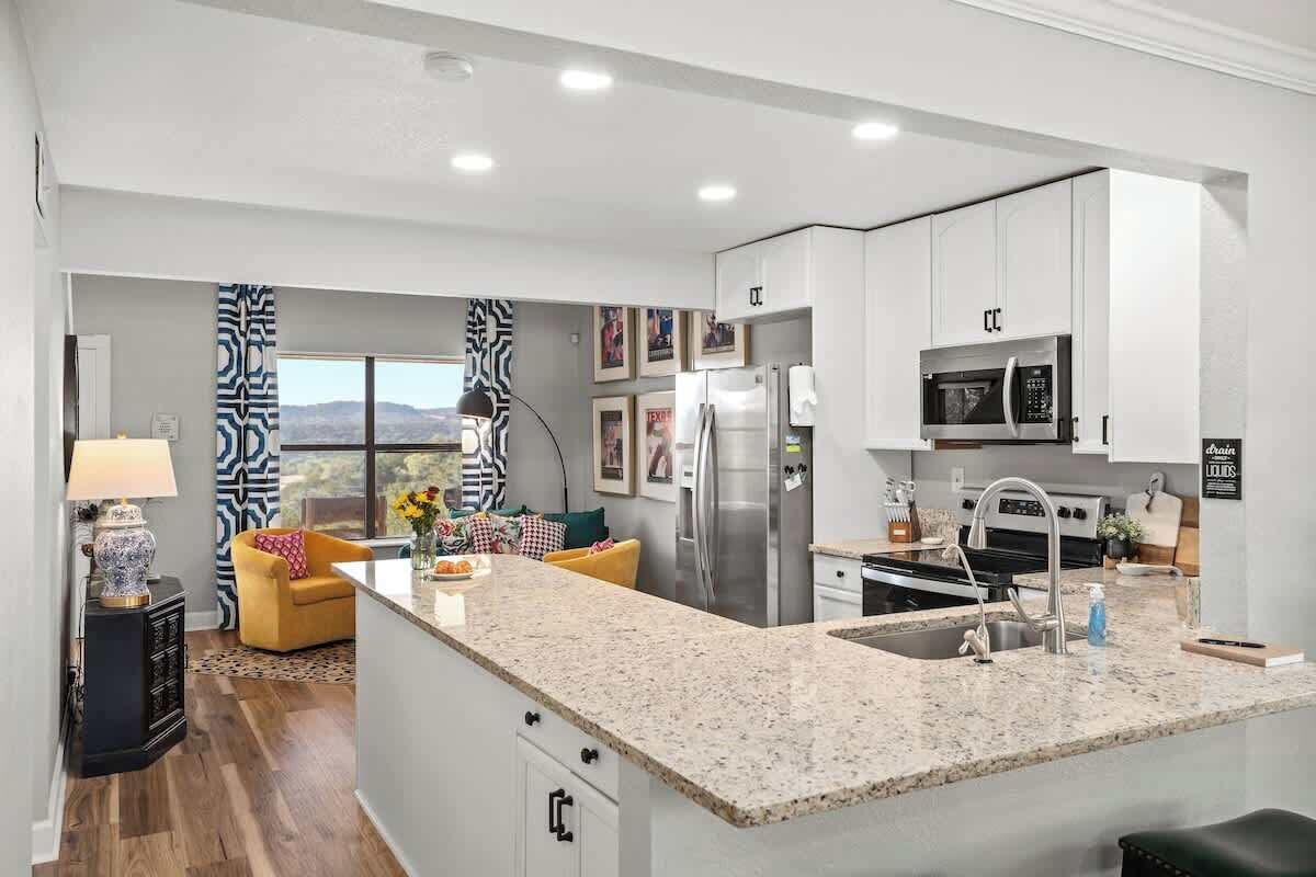 A modern kitchen with white cabinets, a granite countertop, stainless steel appliances, and a view of the mountains.