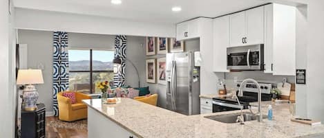 A modern kitchen with white cabinets, a granite countertop, stainless steel appliances, and a view of the mountains.