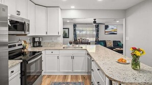 A modern kitchen with white cabinetry, stainless steel appliances, a granite countertop, and a dining area with a view.