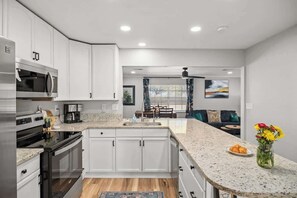 Une cuisine moderne avec des meubles blancs, des appareils en acier inoxydable, un plan de travail en granit et un coin repas offrant une vue agréable.
