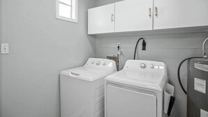 A laundry room with two white washing machines, a cabinet above, and a water heater.