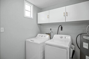 Une buanderie équipée de deux machines à laver blanches, d’un meuble de rangement au-dessus et d’un chauffe-eau.