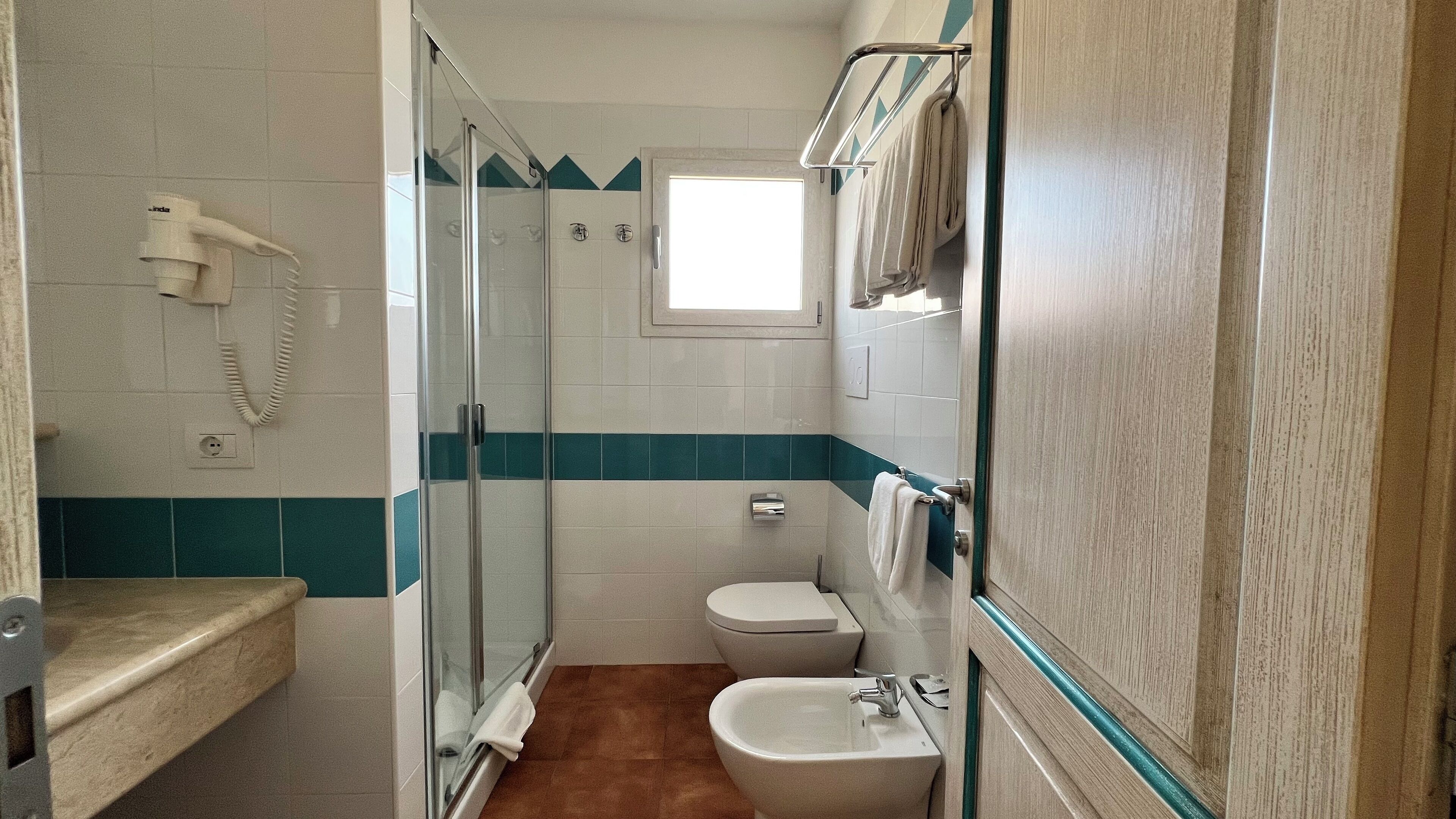 Uma casa de banho com cabine de duche em vidro, sanita, lavatório e um porta-toalhas.