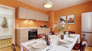A modern kitchen with white cabinets, a dining table set with plates, glasses, and cutlery, and a vase with flowers on the table. - homie stay karmeliten (Würzburg)