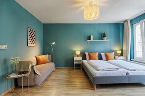 A modern bedroom with a bed, a sofa, a nightstand, a lamp, a wall art piece, and a window with curtains. - homie stay karmeliten (Würzburg)