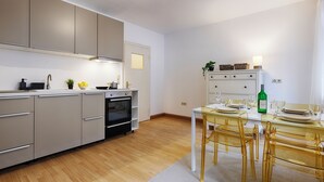 A modern kitchen with a built-in oven, a dining table set for four, and a small island with a sink and storage. - homie stay karmeliten (Würzburg)