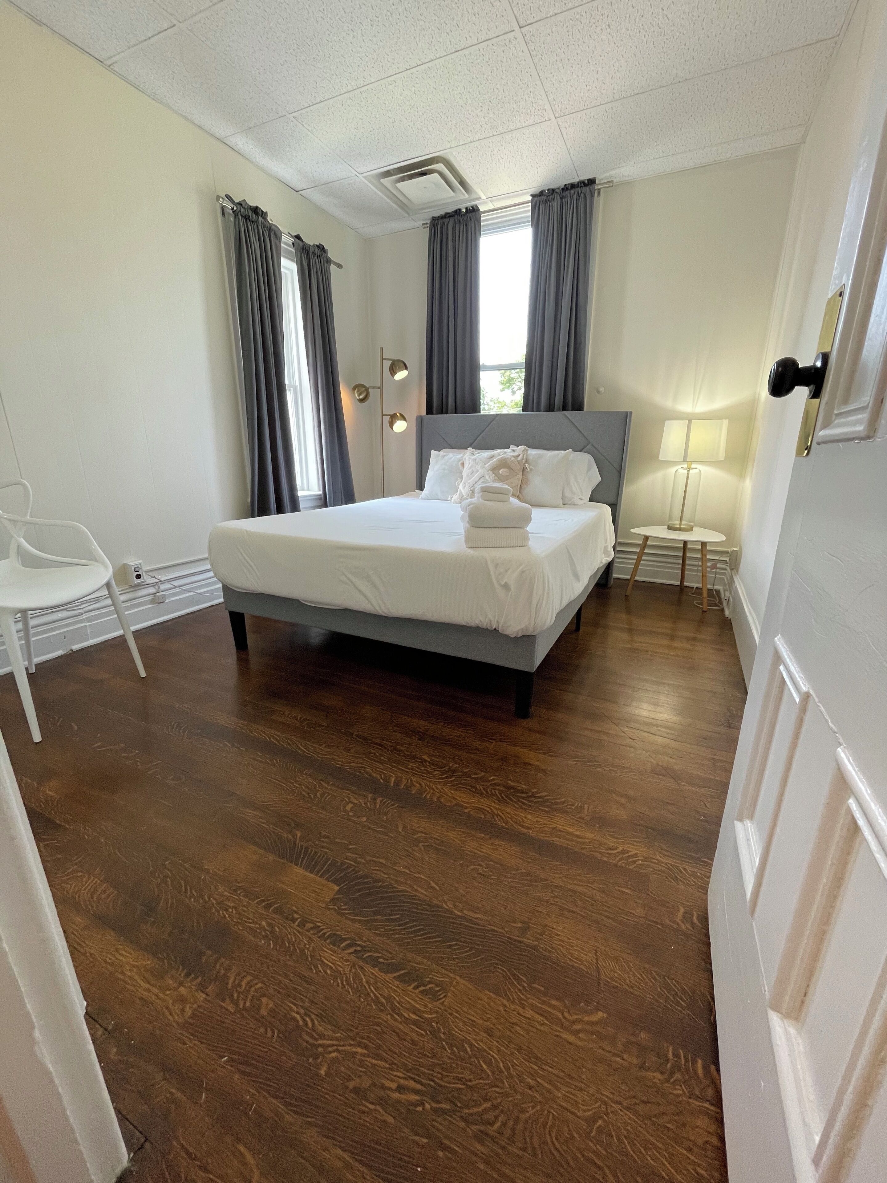 Un dormitorio ordenado con una cama grande, una mesita de noche, una silla y una lámpara.