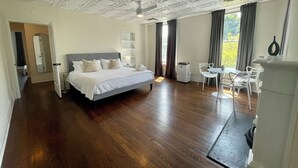 Una habitació d'hotel àmplia amb un llit gran, zona de menjador i vistes a la vegetació.