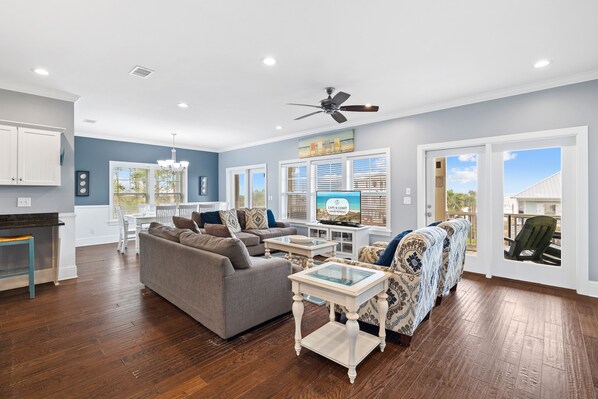 A spacious living room with a grey sofa, a patterned armchair, and a glass-top coffee table.