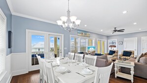 Comedor con una mesa blanca dispuesta para seis personas, rodeada de sillas blancas, y un candelabro colgante.