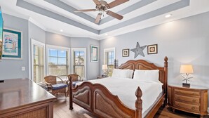 Un dormitorio con cama de madera, sillas de mimbre, ventilador de techo y mesita de noche con lámpara.