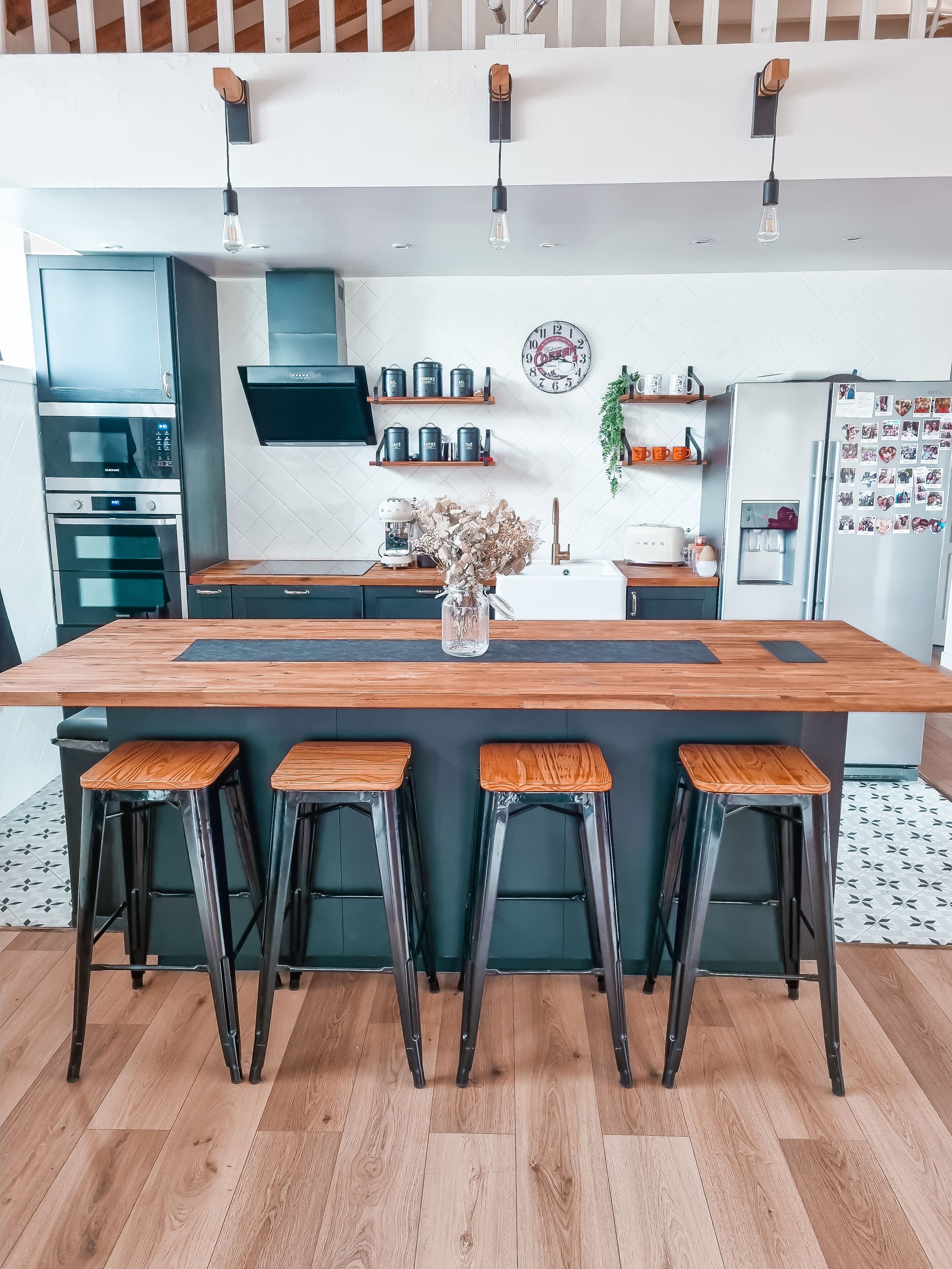 Una cocina moderna con una isla central, taburetes de bar, electrodomésticos de acero inoxidable y un reloj decorativo en la pared.