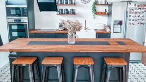 A modern kitchen with a central island, bar stools, stainless steel appliances, and a decorative clock on the wall. - Maison Familiale de 240m2 Proche Paris (Groslay)