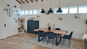 A spacious kitchen with a wooden table, black chairs, and pendant lights. A staircase with a white railing leads to another level. - Maison Familiale de 240m2 Proche Paris (Groslay)