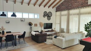 A spacious living area with a wooden ceiling, a dining table with chairs, a sofa, a TV, and a large window with curtains. - Maison Familiale de 240m2 Proche Paris (Groslay)