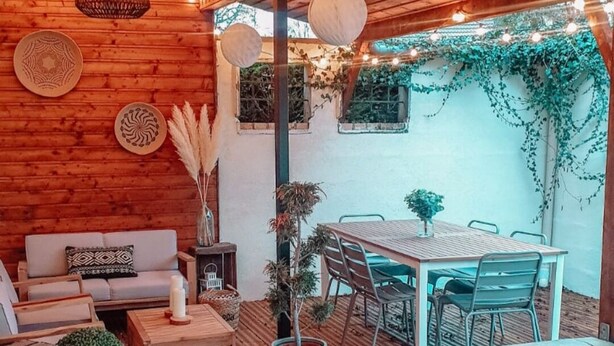 A wooden deck with a dining table and chairs, surrounded by potted plants and a sofa. - Maison Familiale de 240m2 Proche Paris (Groslay)