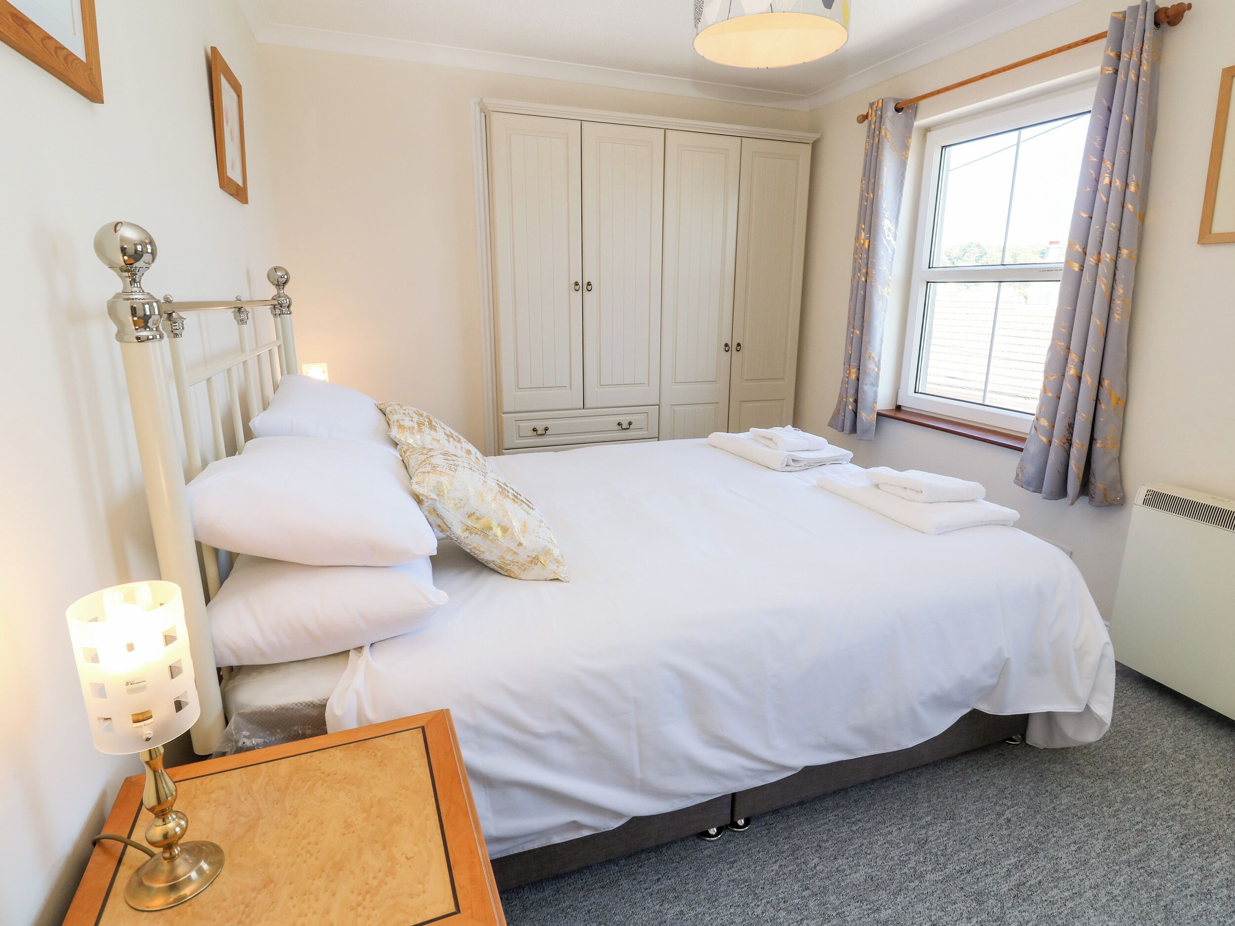 A neatly made bed with white linens, a bedside lamp, and a wooden nightstand.