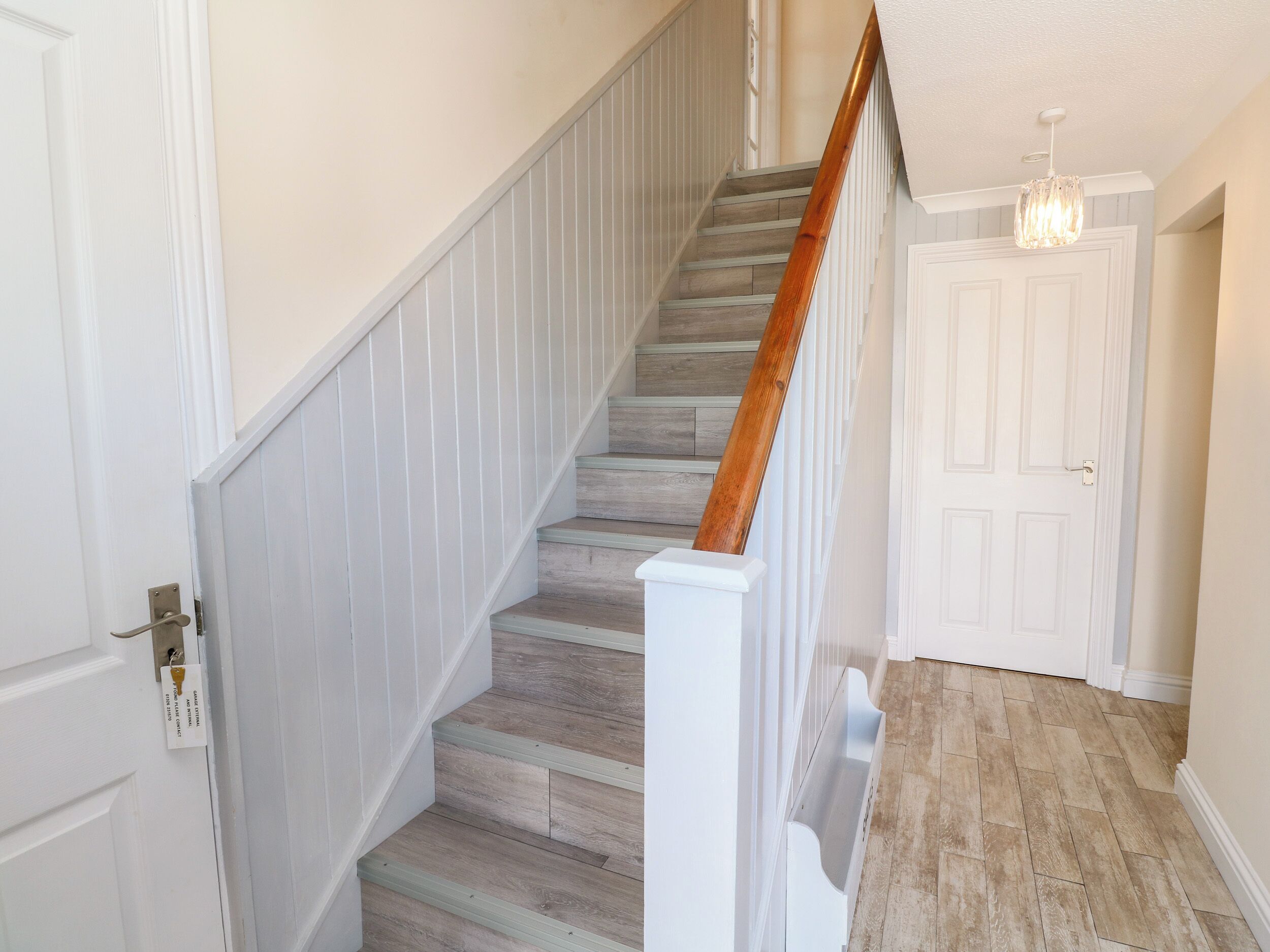 Un escalier avec des marches en bois et une rampe blanche, menant à une porte dotée d’un cadre blanc.